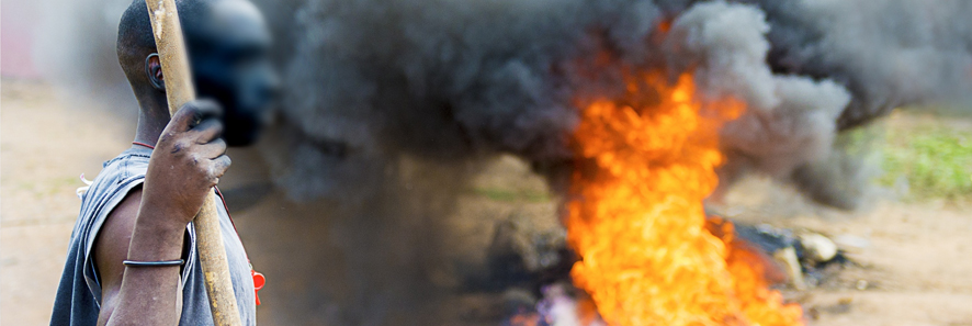 a man with a staff stands next to a fire in the street