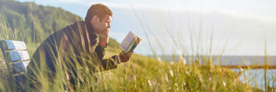 man sits on a bench by the sea reading a book